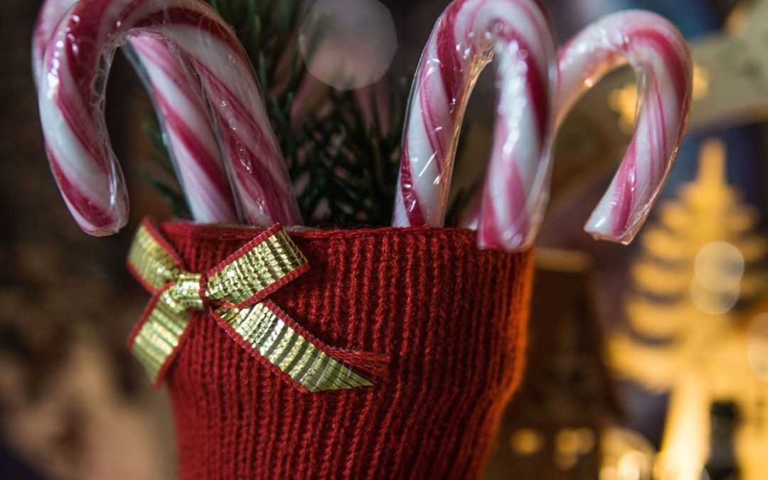 Roter Strickstiefel mit Zuckerstangen und Tannenzweigen vor Lichterschein