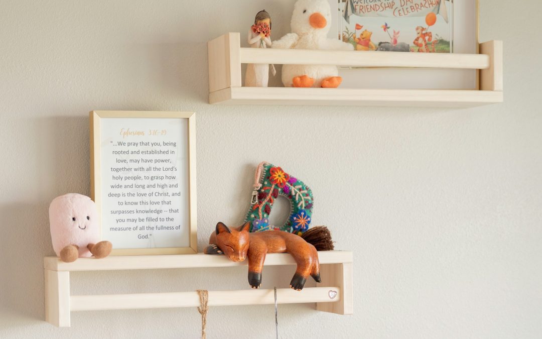Zwei helle Holzregale an einer weissen Wand, darauf Kuscheltiere, ein Bilderrahmen und eine Holzfigur
