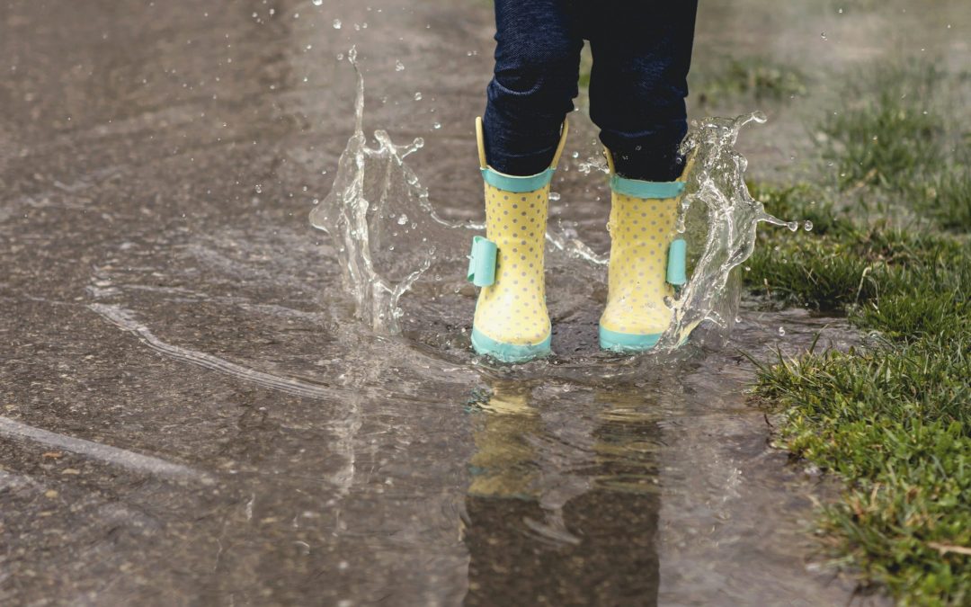 Kinderbeine in gelben Gummistiefeln springen in eine Pfütze