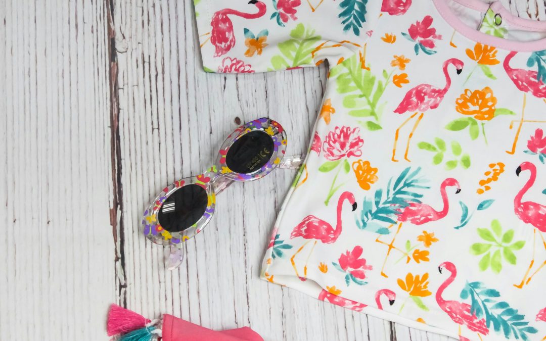 Kindershirt mit Flamingo-Muster und runde Sonnenbrille auf hellem Holz