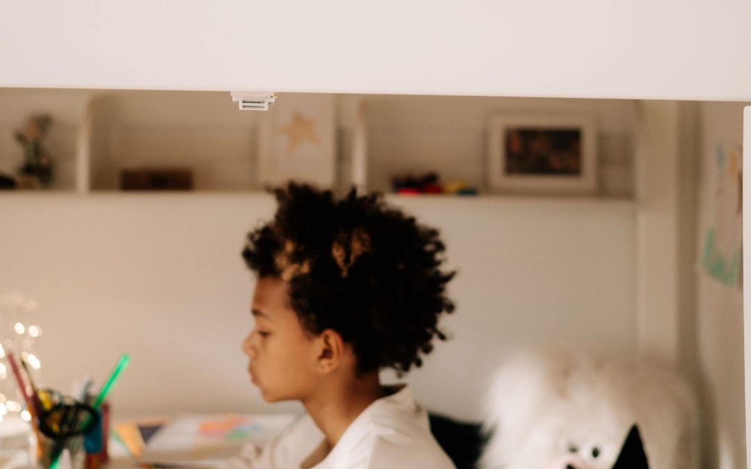 Junge sitzt an einem Schreibtisch unter einem weißen Hochbett, dahinter Regale im Kinderzimmer