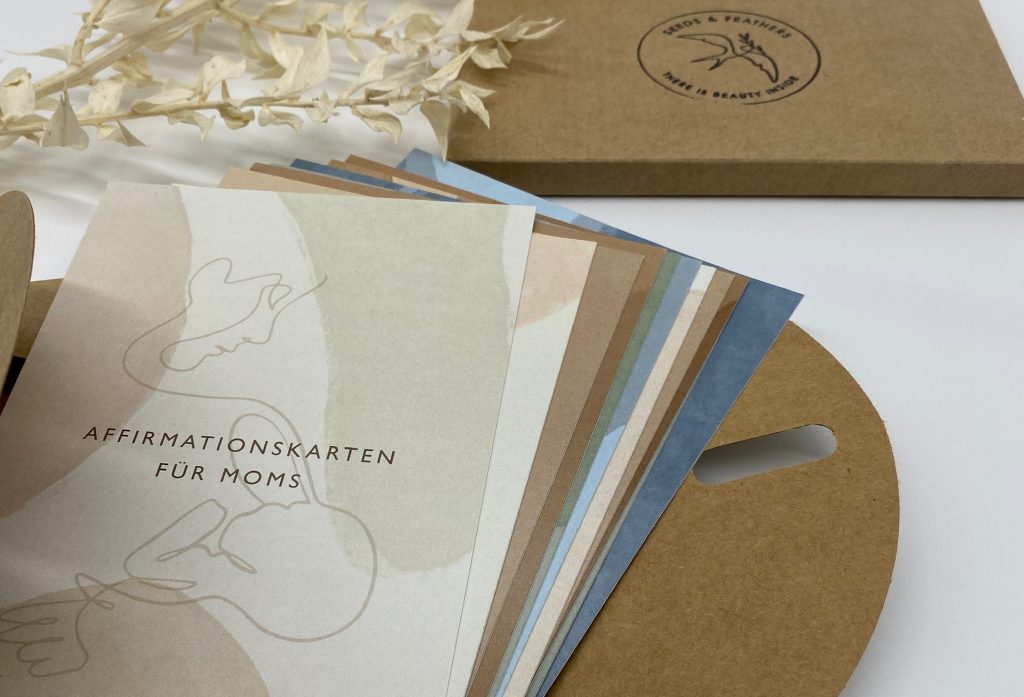 Aufgefächerte Affirmationskarten für Moms neben ihrer Geschenkschachtel von Seeds and Feathers