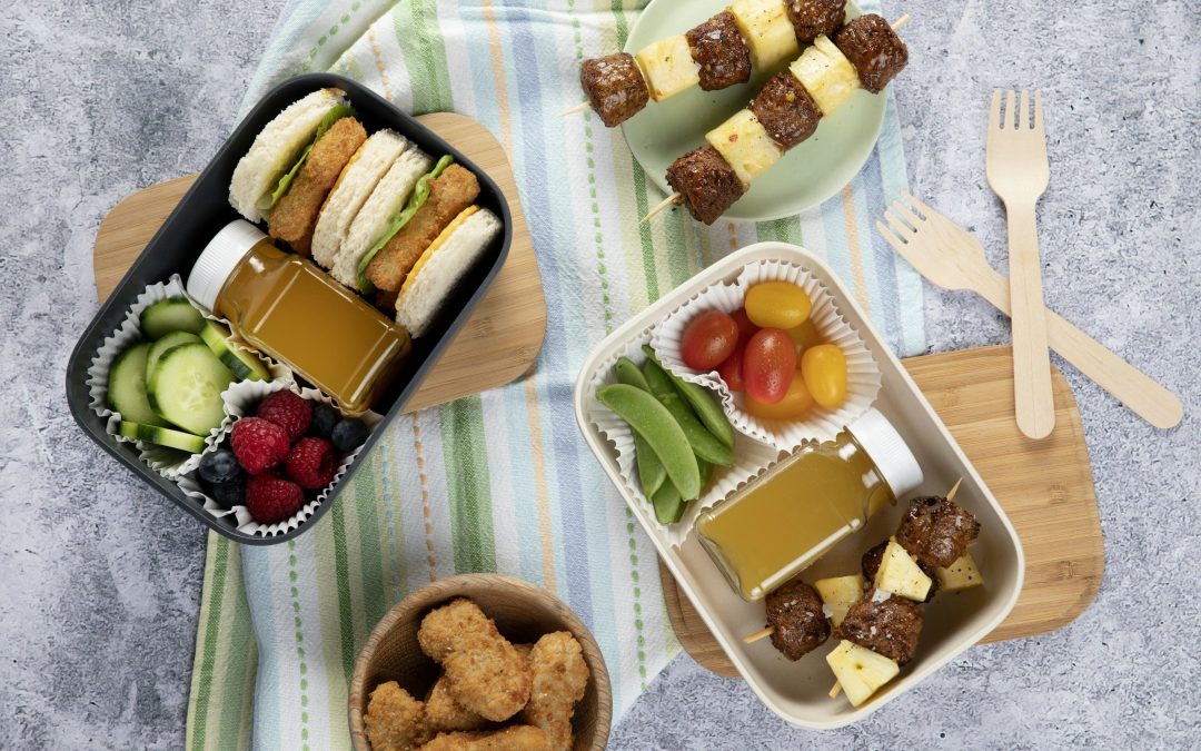 Zwei geöffnete Brotdosen mit Fächern, gefüllt mit Sandwiches, Gurke, Tomaten und Obst