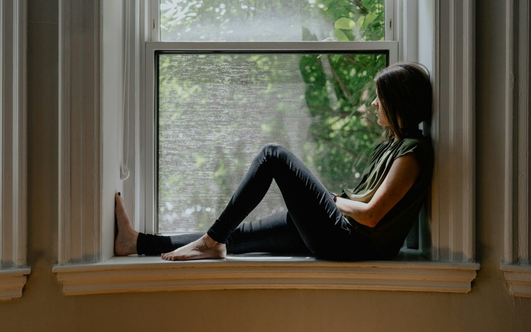 Eine Frau sitzt allein auf einer Fensterbank und schaut nach draußen