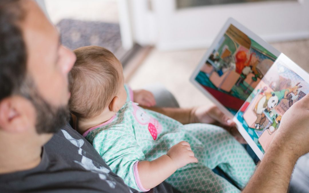 Vater hält sein Baby im Arm und liest ihm ein aufgeschlagenes Bilderbuch vor