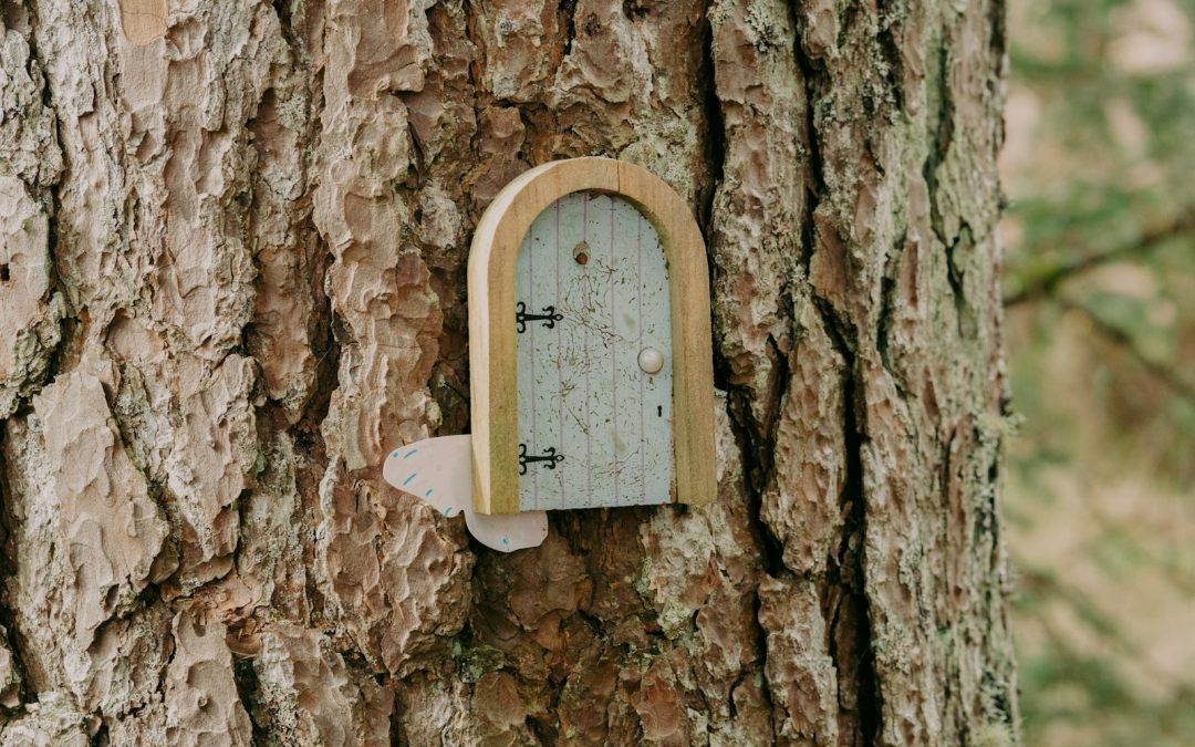 Winzige Holztuer mit Scharnieren und weissem Knauf, an einen Baumstamm gesetzt