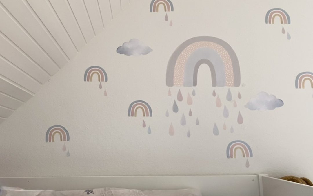 Wandsticker mit Regenbögen und Wolken an einer weißen Dachschräge über einem Kinderbett